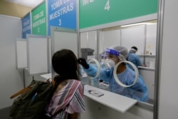 ​ Un trabajador de la salud toma una muestra de hisopo de una mujer en una estación de pruebas rápidas de coronavirus en el Aeropuerto Internacional de Tocumen en la Ciudad de Panamá el 12 de octubre de 2020. ​