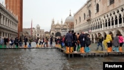 Ljudi hodaju trotoarom na potopljenom Trgu svetog Marka, tokom perioda sezonskih visokih voda u Veneciji, Italija, 29. oktobra 2019.