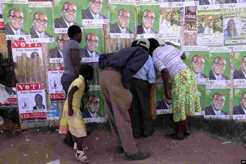 Residents of Epworth look through a hole in a fence covered in campaign posters, Harare, July 30, 2013. 
