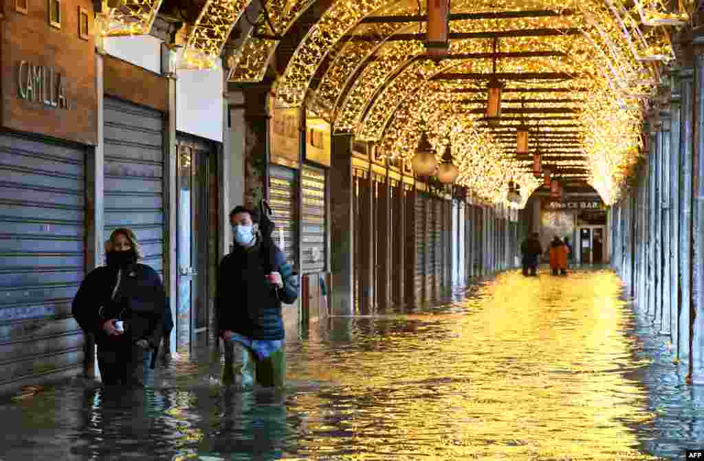 People walk across an arcade by a flooded St. Mark&#39;s Square in Venice.