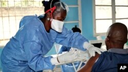 A health care worker from the World Health Organization, left, gives an Ebola vaccination to a front line aid worker who will then vaccinate people who might potentially have the virus, in Mbandaka, Congo, May 30, 2018.