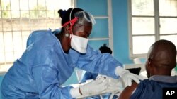 FILE - A health care worker from the World Health Organization, left, gives an Ebola vaccination to a front line aid worker who will then vaccinate people who might potentially have the virus, in Mbandaka, Congo, May 30, 2018.