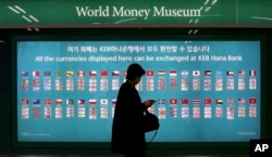 FILE - A woman walks by a board displaying various banknotes issued in the world at a subway station in Seoul, South Korea, Oct. 19, 2017. According to estimates, Chinese sanctions over Seoul's deployment of the THAAD missile defense system might have cost South Korea $7.5 billion in the first 10 months of this year.
