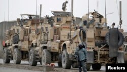 An Afghan policeman stands guard next to NATO armored trucks at the site of a suicide bomb attack in Kabul, Dec.11, 2013. 