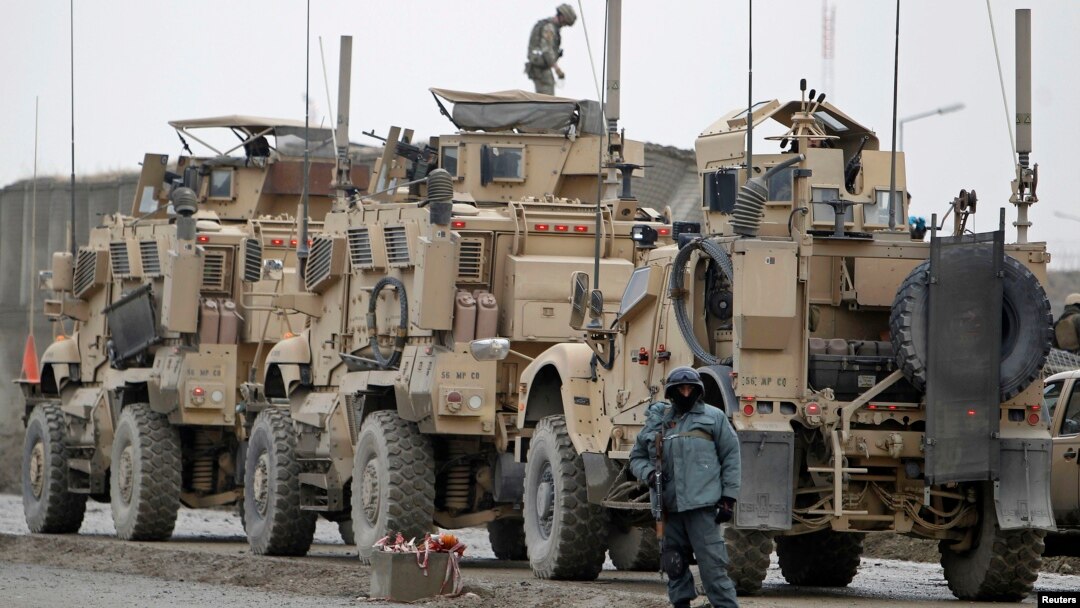 An Afghan policeman stands guard next to NATO armored trucks at the site of a suicide bomb attack in Kabul, Dec.11, 2013. 
