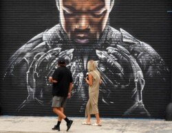 Pedestrians look up at a mural by artist Shane Grammer of late actor Chadwick Boseman's character T'Challa from the 2018 film "Black Panther,", Sept. 8, 2020, in Los Angeles.