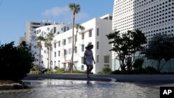 FILE - A woman walks along a flooded street caused by a kind of tide called a king tide on September 28, 2019, in Miami Beach, Florida. (AP Photo/Lynne Sladky, File)