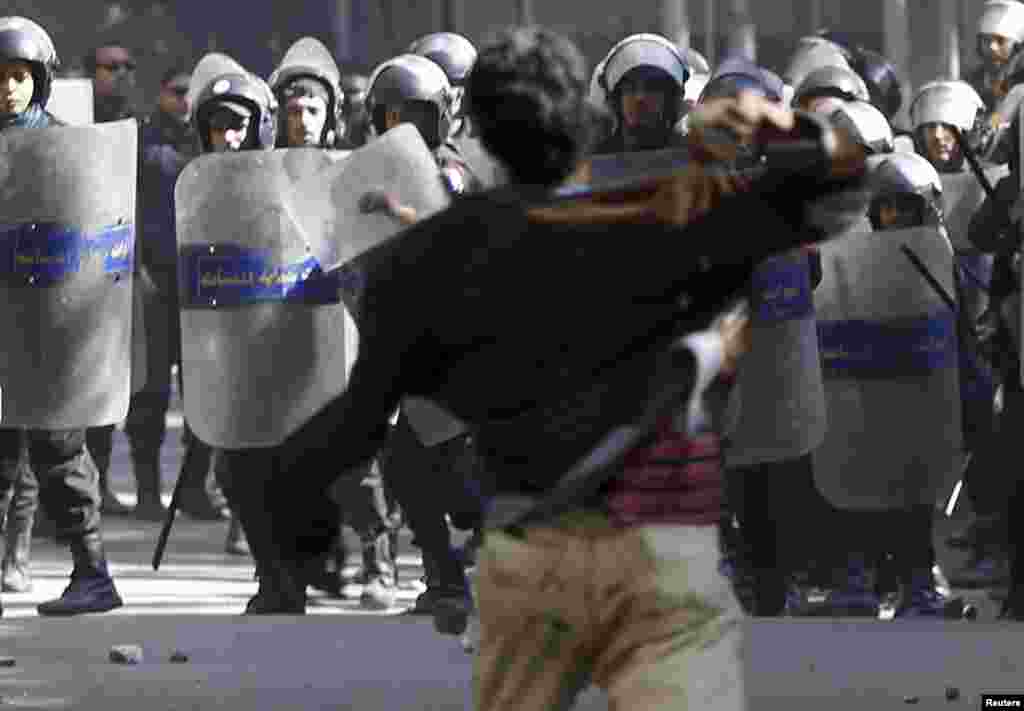 A protester opposing Egyptian President Mohamed Morsi throws a stone at riot policemen during the funeral of activists Mohamed al-Gendy and Amr Saad in Cairo.