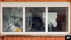 Medical practitioners wearing protective clothing are seen through a window inside an isolated ward on the sixth floor of the the Carlos III hospital in Madrid, Spain on October10, 2014.