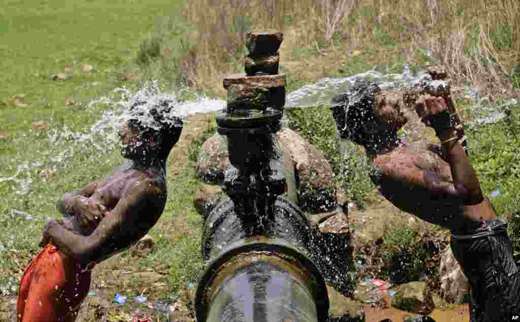 Dua warga India yang tinggal di kawasan kumuh mandi air yang berasal dari pipa air minum yang bocor di pinggiran kota Bhubaneswar, India.