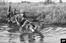 Seorang tentara Vietnam Selatan memegang barang-barang pribadinya di dalam kantong plastik di antara giginya saat unitnya melintasi sungai Delta Mekong yang berlumpur di Vietnam dekat perbatasan Kamboja, 11 Maret 1972. (Foto: AP/Nick Ut)