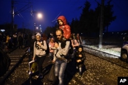 People walk on the railway tracks as they cross the borders from the northern Greek village of Idomeni to southern Macedonia, Sept. 21, 2015.