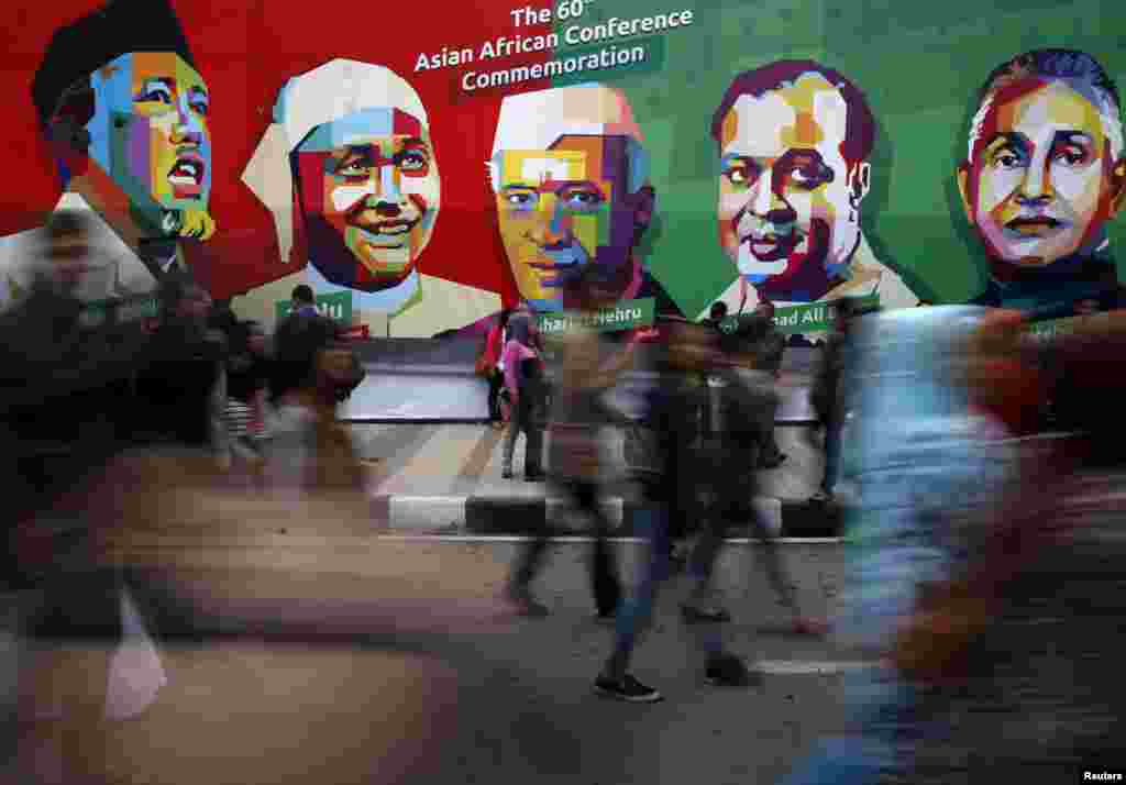 People walk in front a poster of prominent attendees of the 1955 Asian-African Conference on Asia Afrika street in Bandung, Indonesia, April 24, 2015. Leaders of Asian and African nations attended a commemoration ceremony on Friday marking 60 years since the commemoration of the Asian-African Conference.