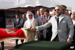 FILE — King Mohammed VI of Morocco waves a Moroccan flag as Moroccan Agency for Solar Energy CEO Mustapha Bakkoury, 2nd right, applauds during the launch of the Noor Ouarzazate 4 solar plant, in Ouarzazate, central Morocco, April 1, 2017.