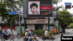 People ride their motorcycles past a digital billboard showing a sketch of the main suspect in Monday's attack on Erawan shrine, in Bangkok, Thailand, August 23, 2015.