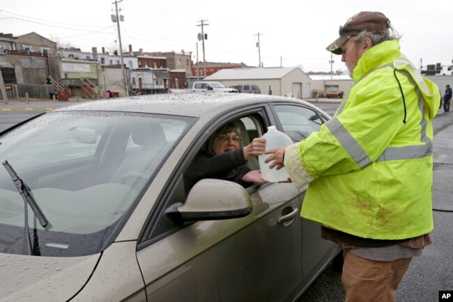 Jeff Vonder, right, an employee of Omaha's Municipal Utilities District, hands Kim O'Connor of Pacific Junction, Iowa, a jug of water he had filled from MUD's emergency water supply tanker, in Glenwood, Iowa, April 3, 2019.
