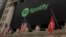 FILE - The Spotify logo hangs on the facade of the New York Stock Exchange with a U.S. and a Swiss flag in New York, April 3, 2018.