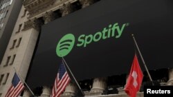 FILE - The Spotify logo hangs on the facade of the New York Stock Exchange with a U.S. and a Swiss flag in New York, April 3, 2018.