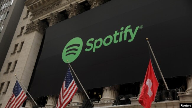 FILE - The Spotify logo hangs on the facade of the New York Stock Exchange with a U.S. and a Swiss flag in New York, April 3, 2018.