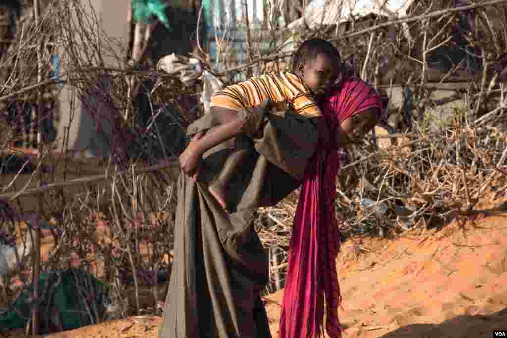 A girl carries a baby boy in a camp in Kismayo, Somalia that is home to both displaced Somalis and returned refugees on September 27, 2016. (J. Patinkin/VOA)