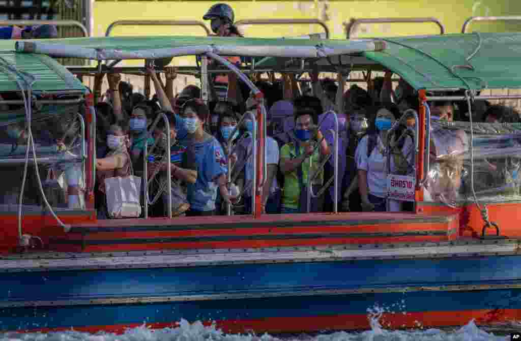 Passengers wearing face masks stand near each other as they ride a boat during the nighttime rush hour in Bangkok, Thailand.