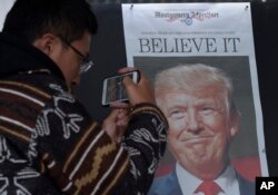 FILE - Zheng Gao of Shanghai, China, photographs the front pages of newspapers on display outside the Newseum in Washington, Nov., 9, 2016, the day after Donald Trump won the presidency.