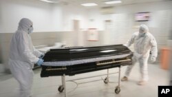 FILE - Funeral house employees drag a coffin on a trolley as they arrive at the University Emergency Hospital morgue to take a COVID-19 victim for burial, in Bucharest, Romania, Nov. 8, 2021.