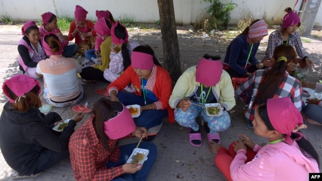 រូបឯកសារ៖ កម្មករ​រោងចក្រ​កាត់​ដេរ​សម្លៀកបំពាក់​កម្ពុជា​កំពុង​ទទួល​ទាន​អាហារ​ពេល​ថ្ងៃ​ត្រង់​នៅ​ក្រោម​ដើម​ឈើ​មួយ​ដើម នៅ​ខាង​មុខ​រោងចក្រ​ដែល​ពួកគេ​ធ្វើការ ភ្នំពេញ ថ្ងៃទី៨ ខែឧសភា ឆ្នាំ២០១៤។