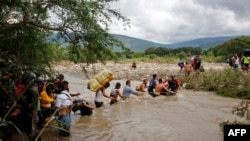 FILE - Migrants use a rope to cross the Tachira River, the natural border between Colombia and Venezuela, as the official border remains closed due to the COVID-19 pandemic in Cucuta, Colombia, Nov. 19, 2020.