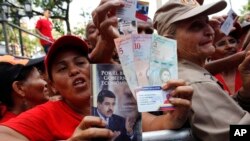 FILE - Pro-government supporters cheer as some hold up new banknotes and patriot identification cards during a rally in Caracas, Venezuela.