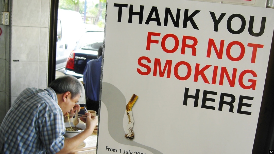 FILE - A man has his lunch behind a poster demarcating a No-Smoking zone in Singapore