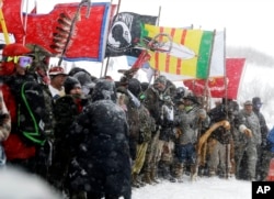 FILE - Military veterans and Native American tribal elders come to a stop for a ceremonial prayer during a march to a closed bridge across from the Dakota Access oil pipeline site in Cannon Ball, North Dakota, Dec. 5, 2016.