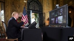 President Donald Trump points to the video screen during a Christmas Eve video teleconference with members of the mIlitary at his Mar-a-Lago estate in Palm Beach, Fla., Dec. 24, 2017.