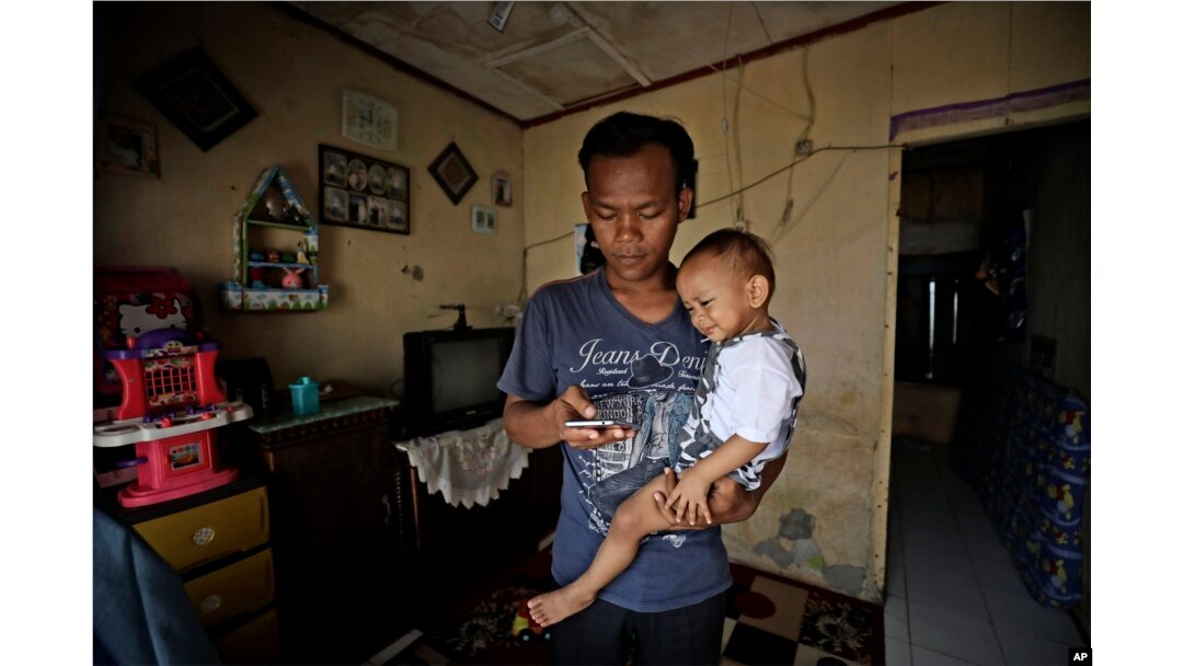 Budi Santosa sedang mengasuh anaknya di rumah kontrakannya di Jakarta, 20 April 2020. (Foto: Dita Alangkara/AP Photo)