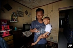 Budi Santosa sedang mengasuh anaknya di rumah kontrakannya di Jakarta, 20 April 2020. (Foto: Dita Alangkara/AP Photo)