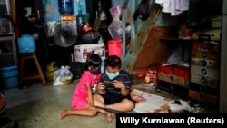 Anak-anak memakai masker bermain dengan smartphone di tengah penyebaran COVID-19 di dalam rumah di kawasan padat penduduk di Jakarta, 1 April 2020. (Foto: REUTERS/Willy Kurniawan)