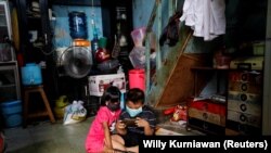 Anak-anak memakai masker bermain dengan smartphone di tengah penyebaran COVID-19 di dalam rumah di kawasan padat penduduk di Jakarta, 1 April 2020. (Foto: Reuters/Willy Kurniawan)