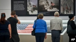 Visitors view the display for the American flag, left, that firefighters hoisted at ground zero in the hours after the 9/11 terror attacks, Sept. 8, 2016, at the Sept. 11 museum in New York. 