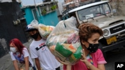 Jóvenes cargan bolsas de alimentos básicos, como pasta, azúcar, harina y aceite de cocina, proporcionados por un programa de asistencia alimentaria del gobierno, para entregarlos en el barrio Santa Rosalía de Caracas, el 10 de abril de 2021. 