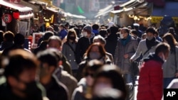 People wearing face masks to protect against the spread of the coronavirus walk though a shopping street Dec. 31, 2020, in Tokyo. 