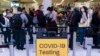 FILE - Travelers wait in line for screening near a sign for a COVID-19 testing site at the Los Angeles International Airport in Los Angeles, Nov. 24, 2021. 