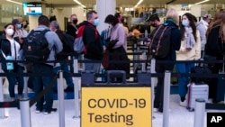 FILE - Travelers wait in line for screening near a sign for a COVID-19 testing site at the Los Angeles International Airport in Los Angeles, Nov. 24, 2021. 
