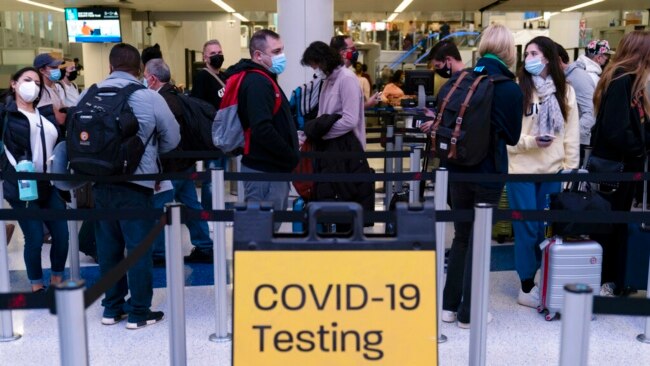 FILE - Travelers wait in line for screening near a sign for a COVID-19 testing site at the Los Angeles International Airport in Los Angeles, Nov. 24, 2021.