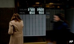 FILE - A woman looks at a sign announcing the price of the U.S. dollar and Brazilian real, in exchange for Argentine pesos, at a money exchange house in Buenos Aires, Argentina, Sept. 3, 2018.