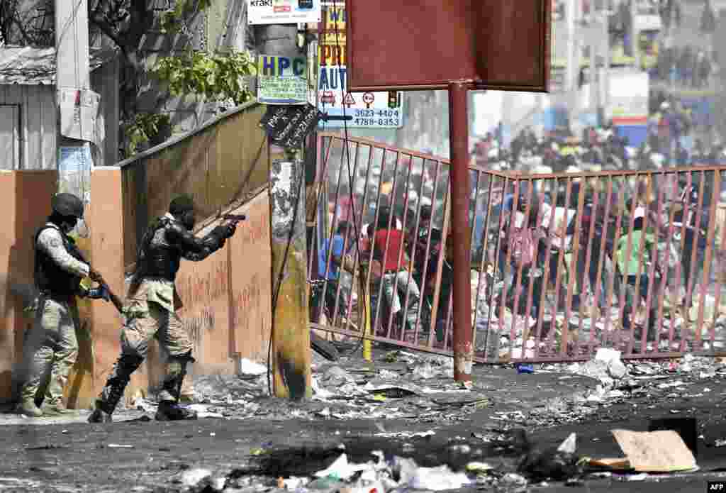 A member of the Haitian police points his gun at people to avoid looting in shops in Delmas, a commune near Port au Prince during protests against the rising price of fuel.