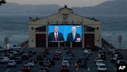 People watch from their vehicles as President Donald Trump, on left of video screen, and Democratic presidential candidate former Vice President Joe Biden speak during a presidential debate watch party at Fort Mason Center in San Francisco, Oct.
