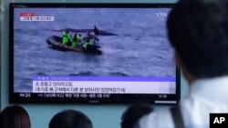 People watch a TV news program showing South Korean Coast Guard officers search for missing passengers after a fishing boat capsized in the water off north of the resort island of Jeju, at Seoul Railway Station in Seoul, Sept. 6, 2015