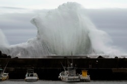 Men look at fishing boats as surging waves hit against the breakwater while Typhoon Hagibis approaches at a port in town of Kiho, Mie Prefecture, Japan, Oct. 11, 2019.