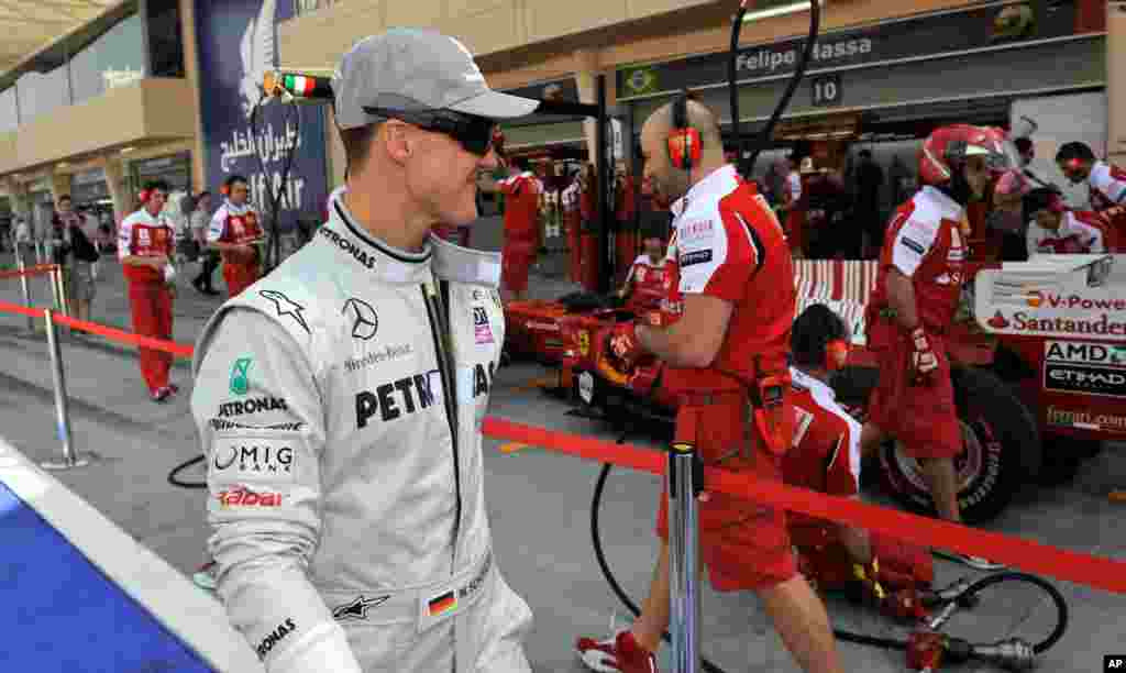 Michael Schumacher looks to a Ferrari car as he walks through the pit lane before the first practice session at the Formula One Bahrain International Circuit in Sakhir, March 12, 2010. 