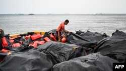 Seorang personel garda pantai sedang menata penghalang tumpahan minyak untuk persiapan pengerahan di sebuah pelabuhan di Limay, Bataan, 25 Juli 2024. (Foto: Jam Sta Rosa/AFP)